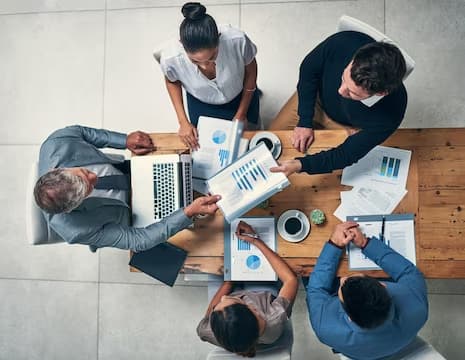 5 pessoas sentadas em volta da mesa durante uma reunião de negócios